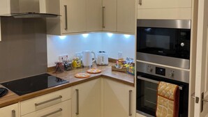 A compact kitchen with white cabinets, a black induction cooktop, a stainless steel oven, and a microwave. - Kingmaker House - Luxury 3 Bedrooms, Driveway, Garage, Garden, M1 (Northampton)