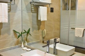 A modern bathroom with a large mirror, a sink, and a toilet. There are towels hanging on a rack and a potted plant on the counter. - Hequn Hotel (Xinchang)