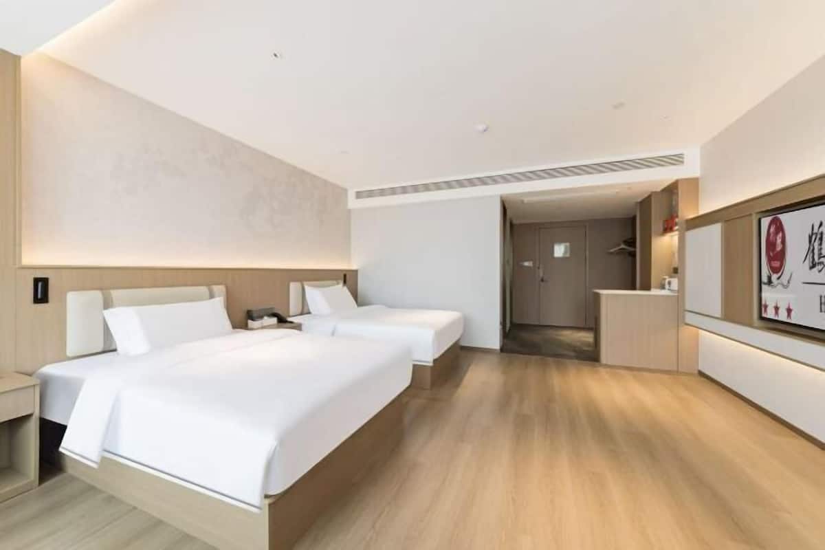 A hotel room with two beds, a desk, a mirror, and a small bathroom.