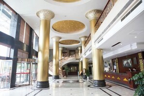 A spacious lobby with high ceilings, large golden columns, and a grand staircase. - Hequn Hotel (Xinchang)