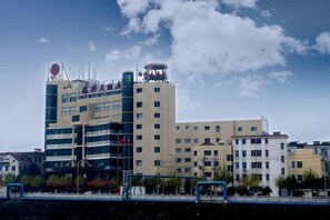 A multi-story hotel with a modern architectural design, featuring a prominent circular logo on the top of the building. - Hequn Hotel (Xinchang)