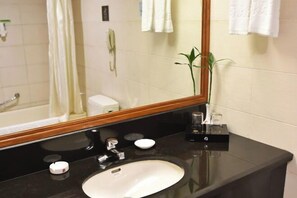 A bathroom with a black countertop, a white sink, a mirror, a plant, and a telephone. - Hequn Hotel (Xinchang)