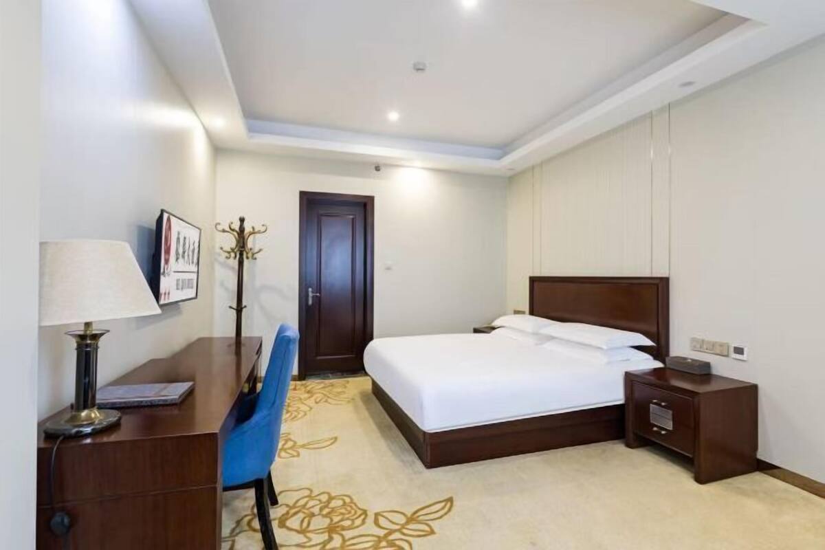 A hotel room with a bed, bedside table, lamp, chair, and a door.