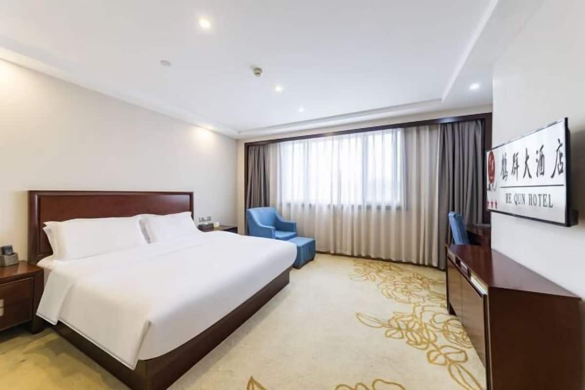 A hotel room with a large bed, a desk, a chair, and a window with curtains.
