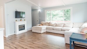 A living room with a fireplace, a television mounted above it, a large window, and a beige sectional sofa.
