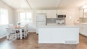 A kitchen with white cabinetry, a central island, a dining table with chairs, and a chandelier.