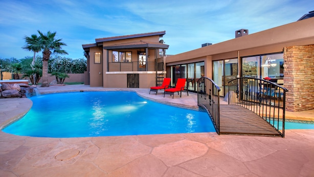 Une maison moderne avec une piscine, des chaises rouges et une terrasse en pierre.