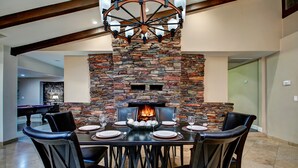Un espace repas agrémenté d’une cheminée en pierre, d’une table de billard et d’un lustre.