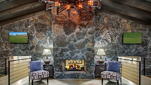 Une cheminée en pierre avec un feu de bois, deux fauteuils à motifs et un téléviseur fixé au mur.