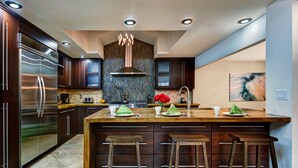 Une cuisine moderne avec des meubles de couleur bois foncé, des appareils électroménagers en acier inoxydable et un grand îlot central doté de tabourets.