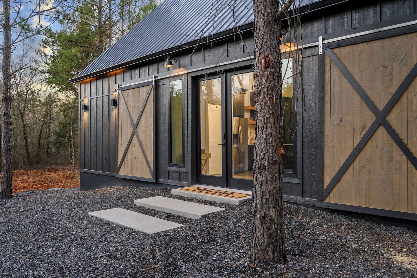 Une cabane rustique avec de grandes portes en bois, un toit en métal et une allée gravillonnée.