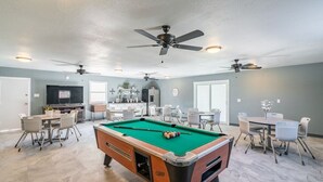 Una habitación amplia con mesa de billar, comedor y ventiladores de techo.