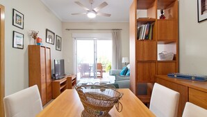 A dining area with a wooden table, white chairs, a ceiling fan, and a bookshelf with books and a basket.