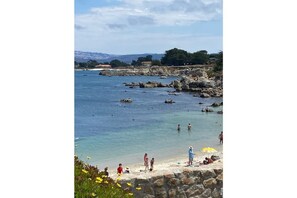 Uma praia costeira com formações rochosas, água cristalina e pessoas aproveitando a praia.