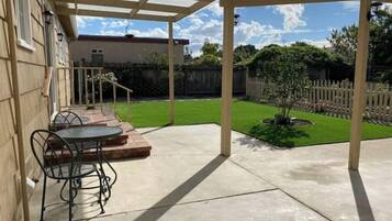 A covered patio with a table and chairs, a small lawn, and a wooden fence.