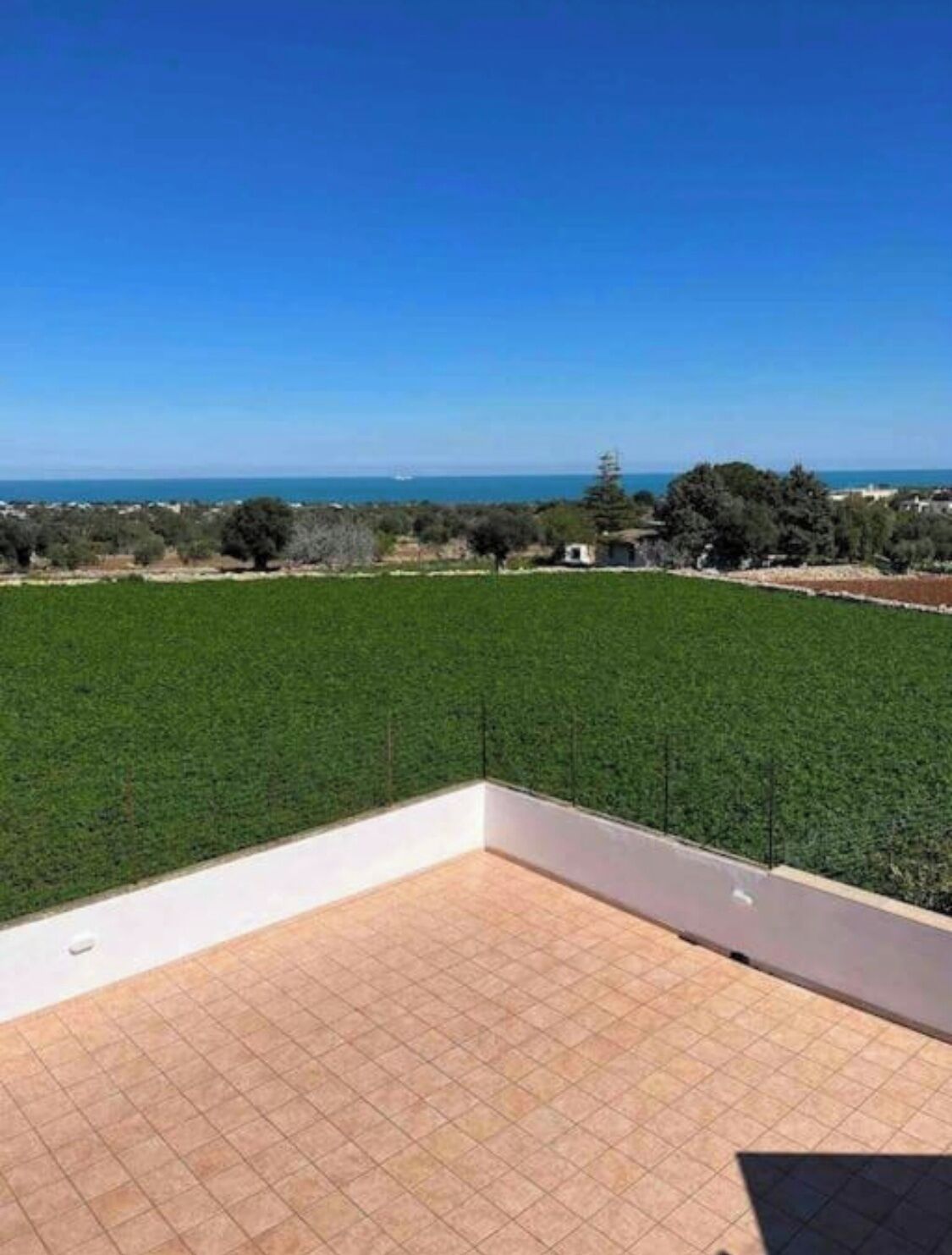 Eine Terrasse mit Blick auf ein grünes Feld und das Meer.