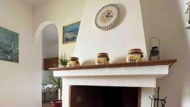 Una sala de estar con chimenea, un reloj en la pared y un taburete pequeño.