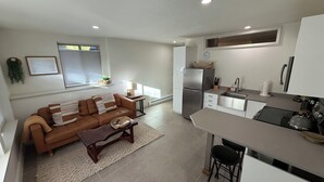 A modern kitchen with a refrigerator, stove, and sink. There is a brown leather sofa and a small table with a basket.