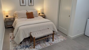 A neatly arranged bedroom with a bed, bedside tables, a bench, and wall-mounted artwork.