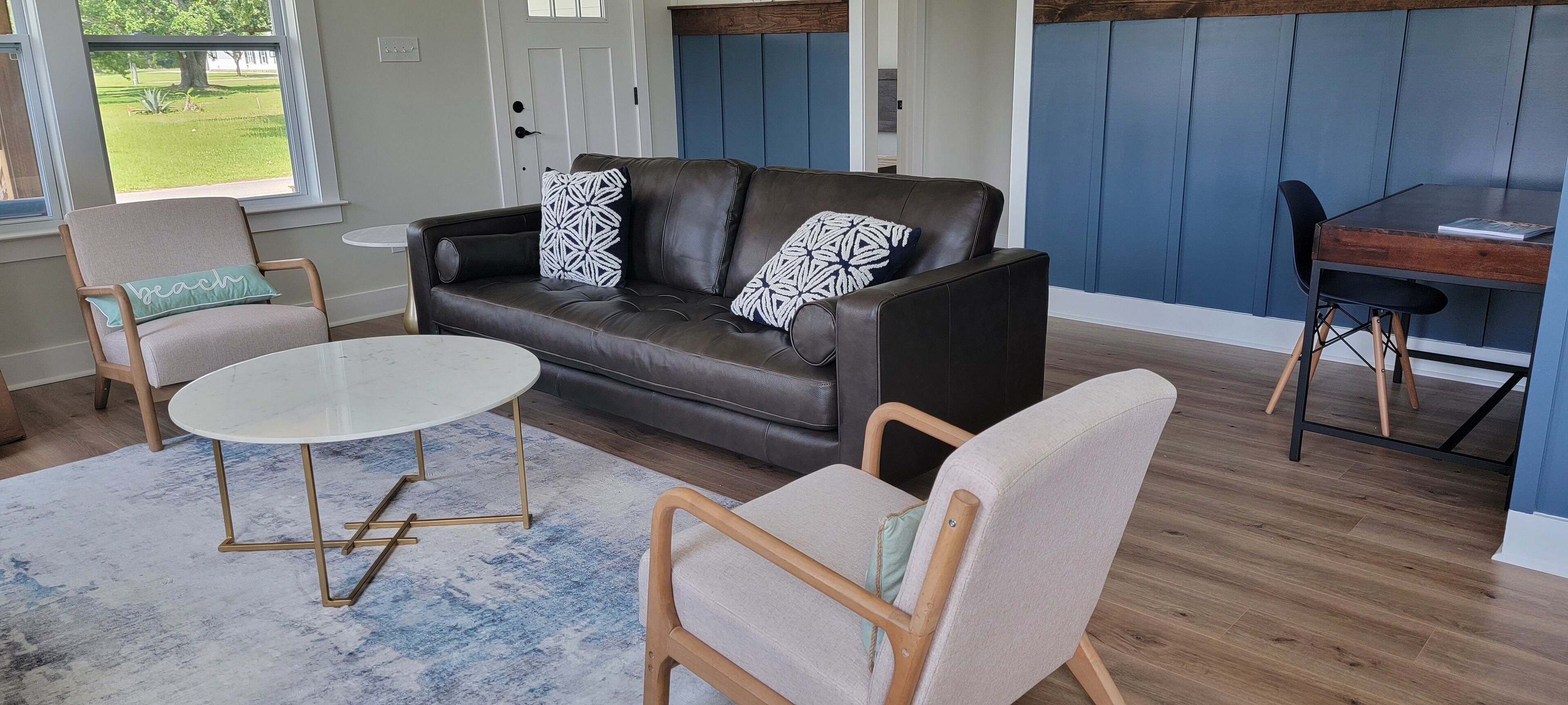 A living room with a dark leather sofa, two armchairs, a round coffee table, and a dining table with chairs.