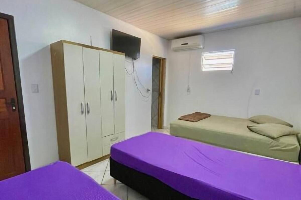 A room with two beds, a wardrobe, a television, and an air conditioning unit.