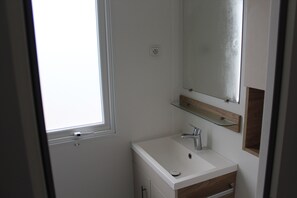Un baño con un lavabo blanco, un espejo y una ventana.
