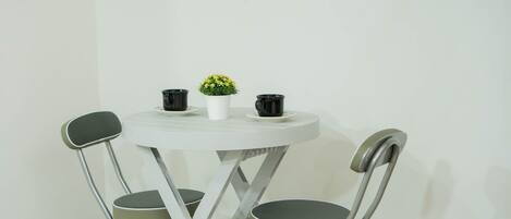 A small round table with a white surface, two black cups, and a small potted plant with yellow flowers.