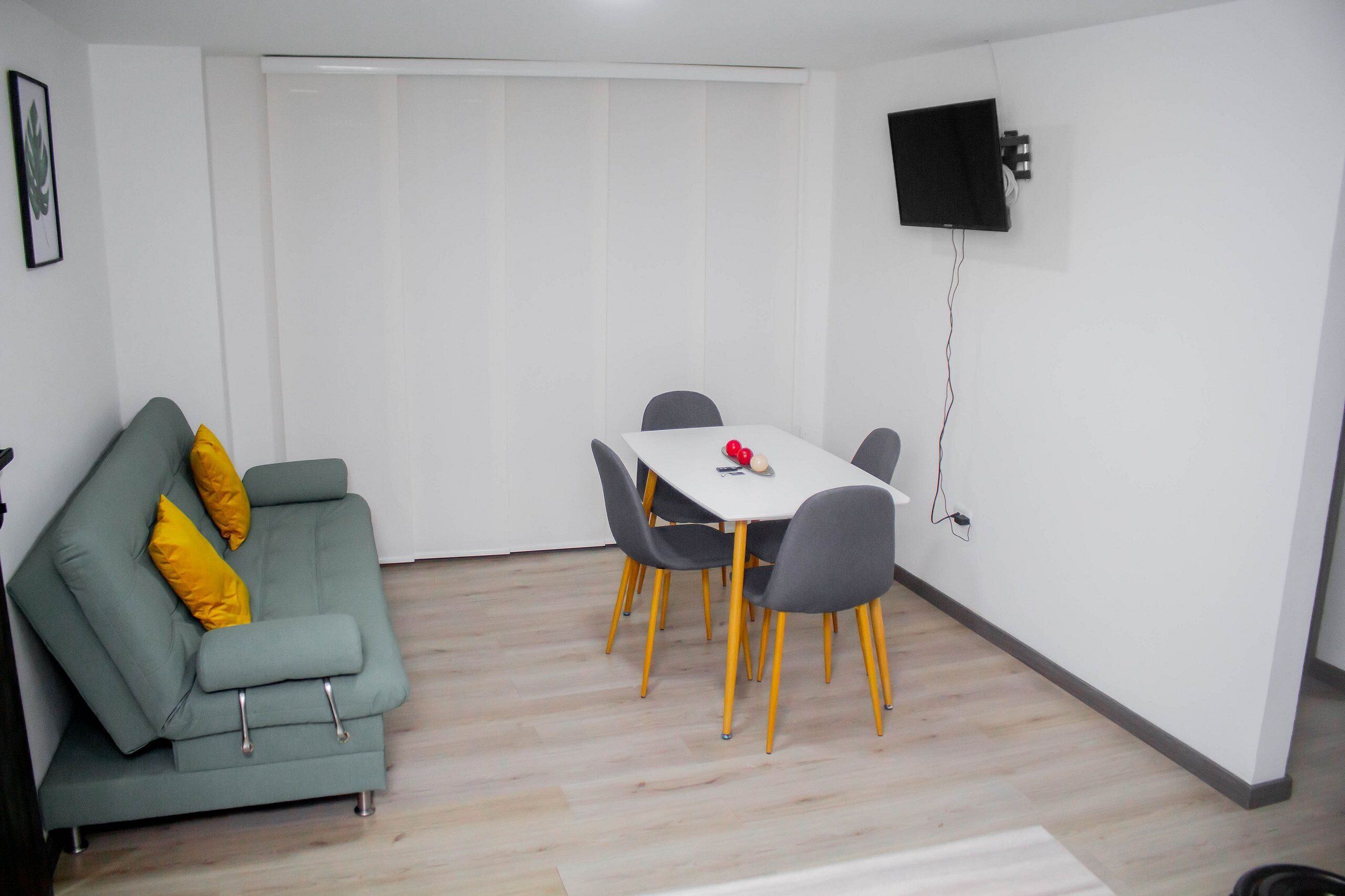 A living room with a grey sofa, yellow cushions, a dining table with chairs, and a mounted TV.