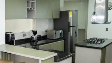 A compact kitchen with a refrigerator, microwave, gas stove, and a coffee maker.