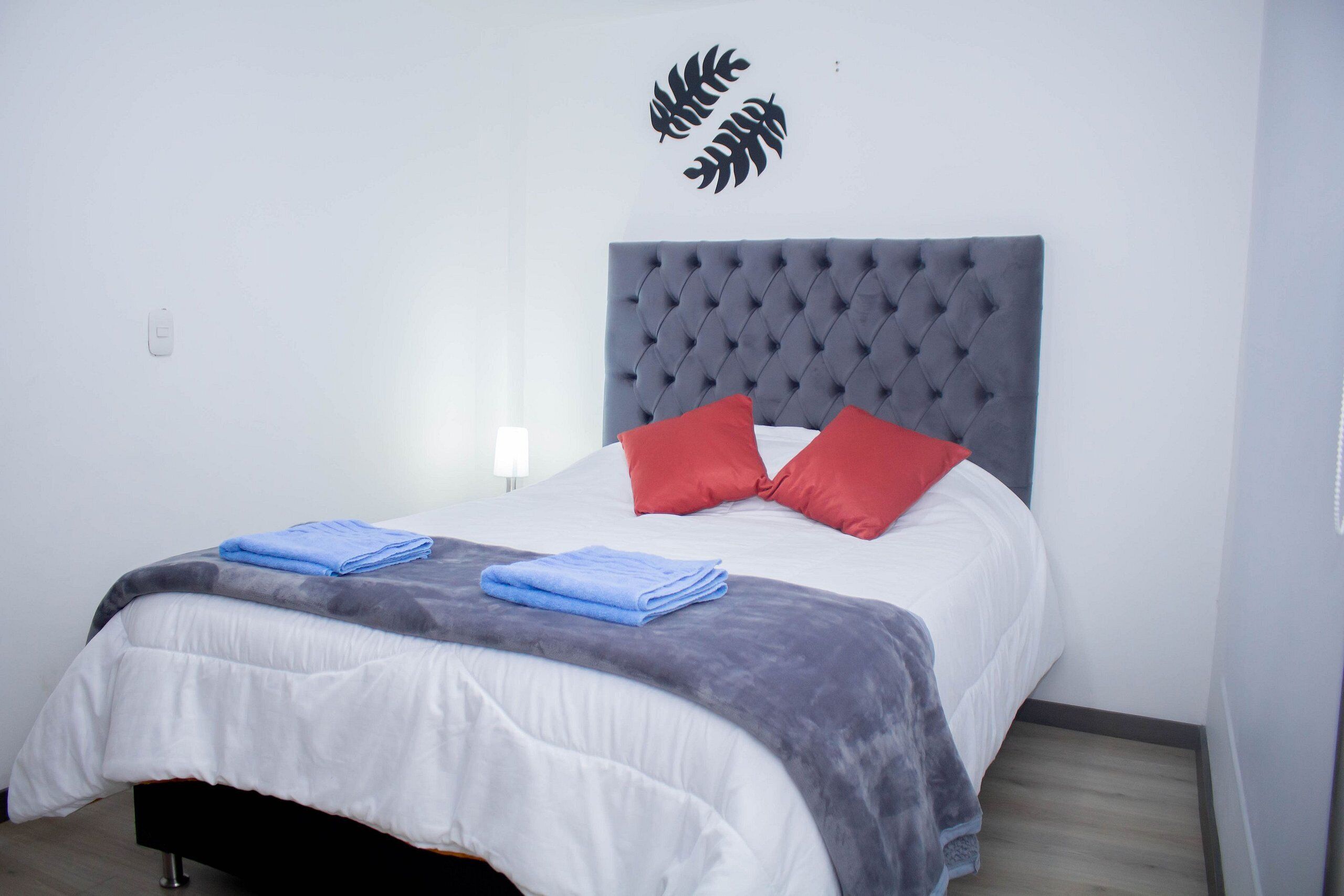 A neatly made bed with a grey headboard, white and grey bedding, and two red pillows.