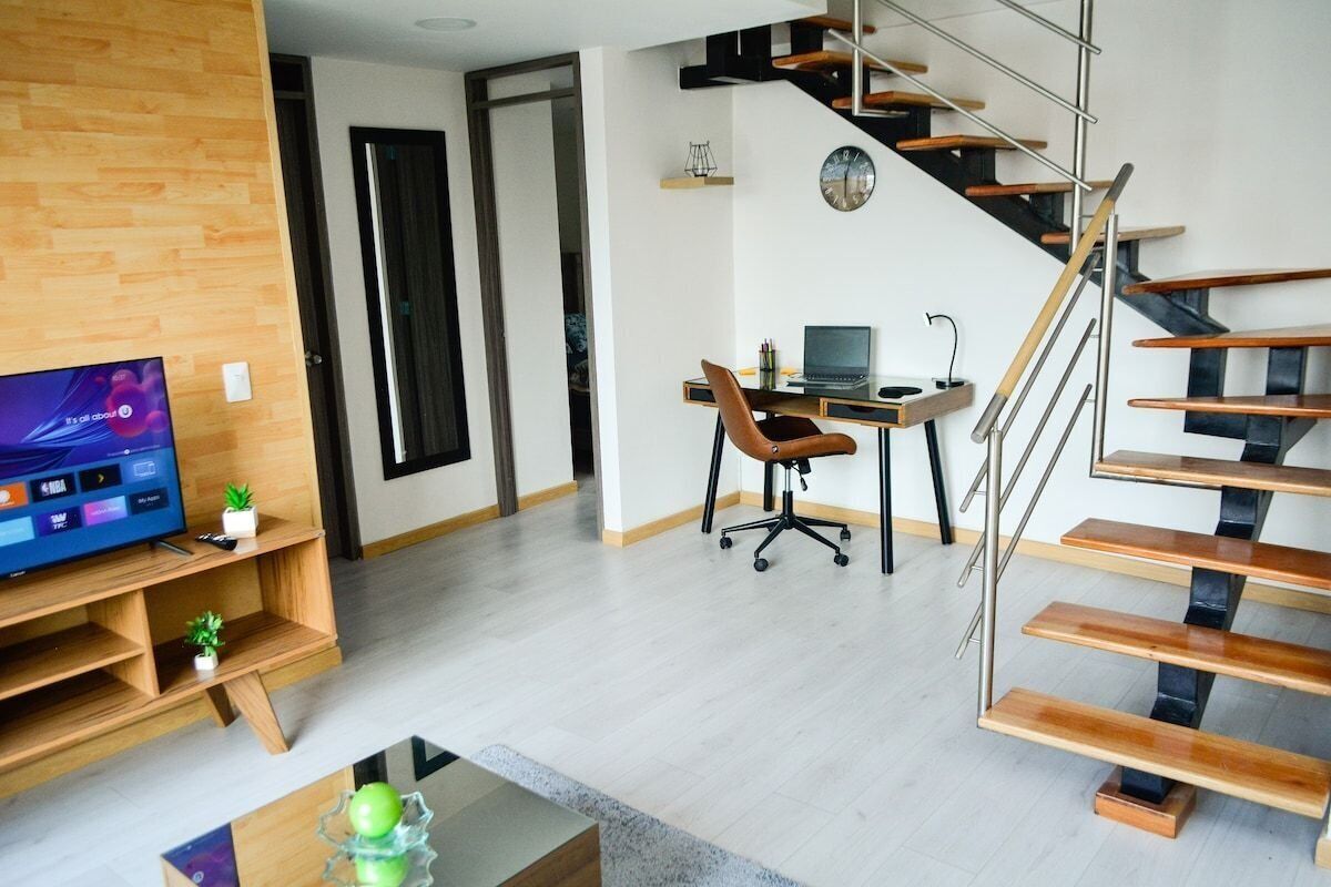 Una sala de estar moderna con un mueble de televisión de madera, una mesa de centro de cristal y una escalera con escalones de madera y barandilla de metal.