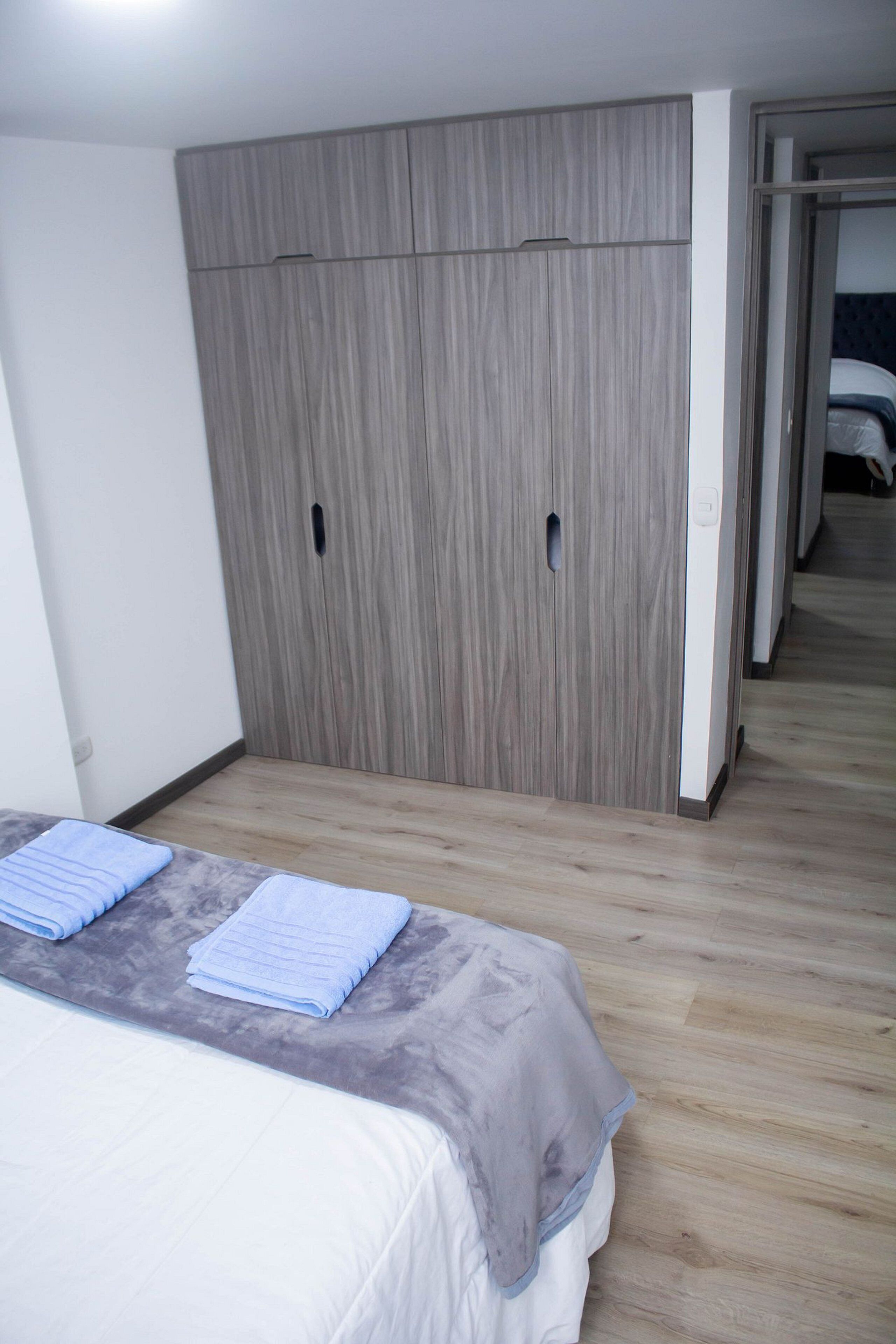 Quarto com cama, guarda-roupa e porta que dá para outro cômodo.
