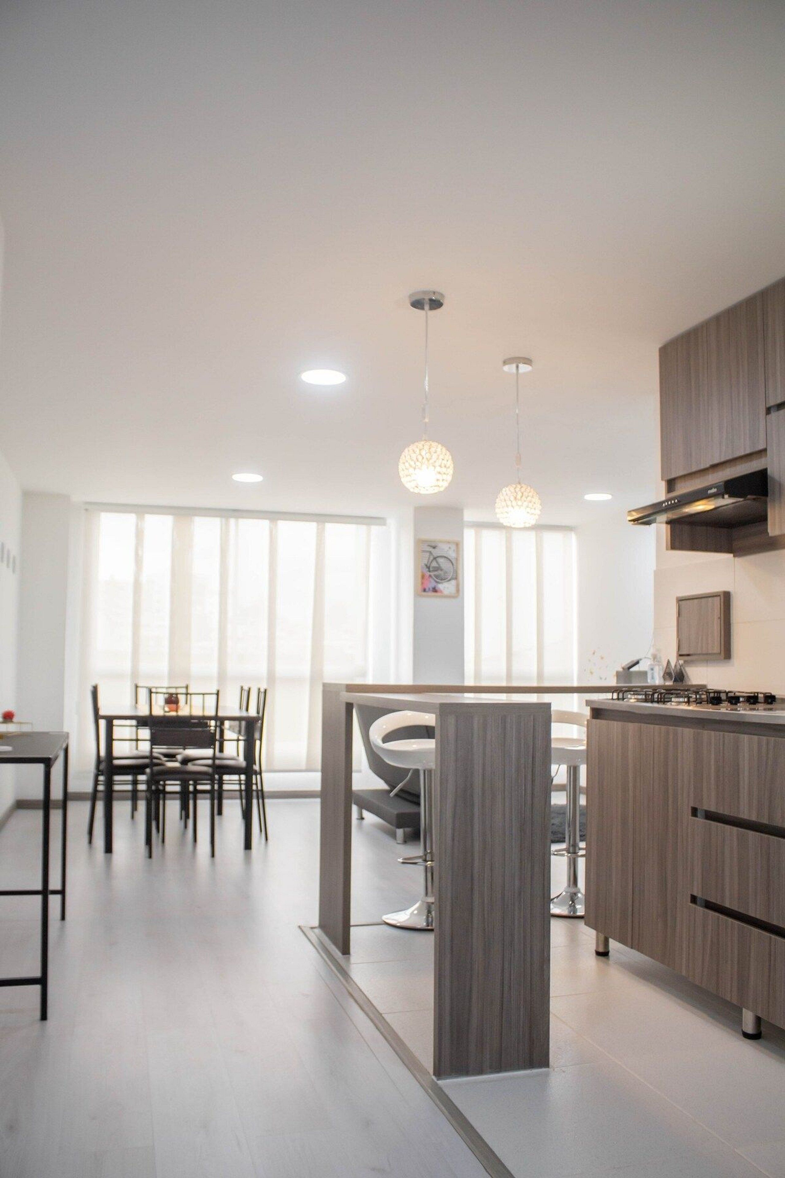Cocina moderna con comedor, que incluye una isla central, luces colgantes y un amplio ventanal que proporciona luz natural.