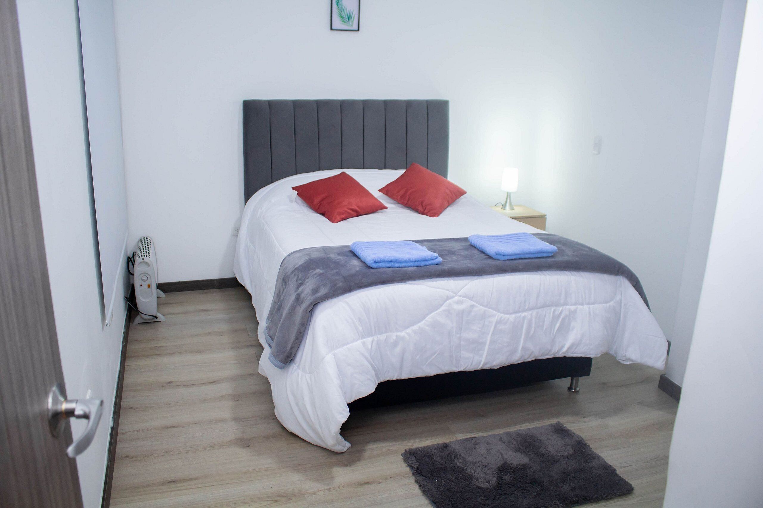 Een slaapkamer met een bed, een nachtkastje, een lamp en een klein vloerkleed.