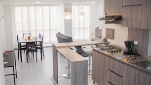 A modern kitchen with a dining area, featuring a central island, bar stools, and a built-in stove. - EDIFICIO CAMILA (Manizales)
