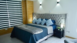 A bedroom with a tufted headboard, a bed with blue bedding, a nightstand with a lamp, and a round rug. - EDIFICIO CAMILA (Manizales)