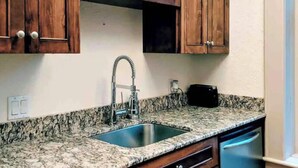 A kitchen with wooden cabinets, a granite countertop, a stainless steel sink, and a window with a view.