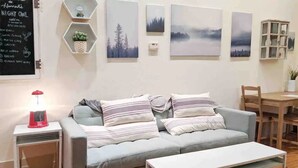 A modern living room with a grey sofa, striped cushions, a white coffee table, and a red lamp. There are hexagonal shelves with plants and artwork on the wall.