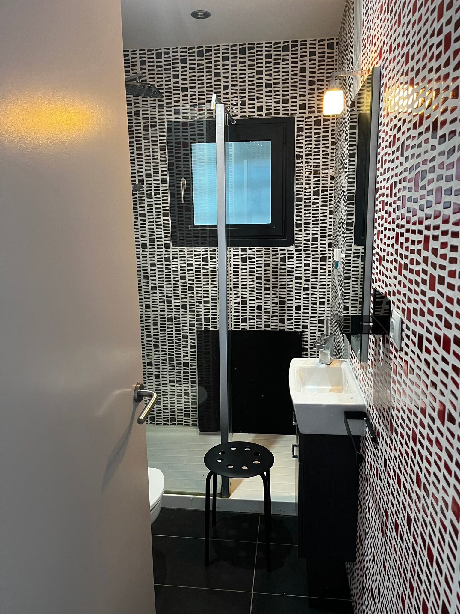 A modern bathroom with a black and white patterned wall, a white sink, and a black toilet.