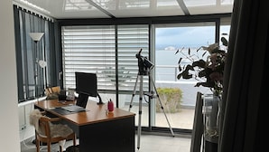 Un salon moderne avec une grande fenêtre, un bureau, une chaise, un télescope et un tapis moelleux.