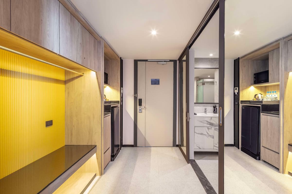 A modern hallway with wooden paneling, a kitchen area with a microwave and refrigerator, and a bathroom with a mirror and sink.