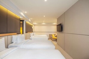 Una habitación de hotel con tres camas, un televisor y una silla amarilla.