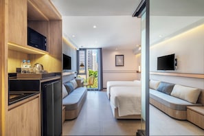 A modern hotel room with a kitchenette, a bed, a seating area, and a TV.