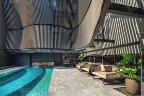 A modern building with a curved facade, a swimming pool, and outdoor seating. - Best Western Ratchada Hotel (Bangkok)
