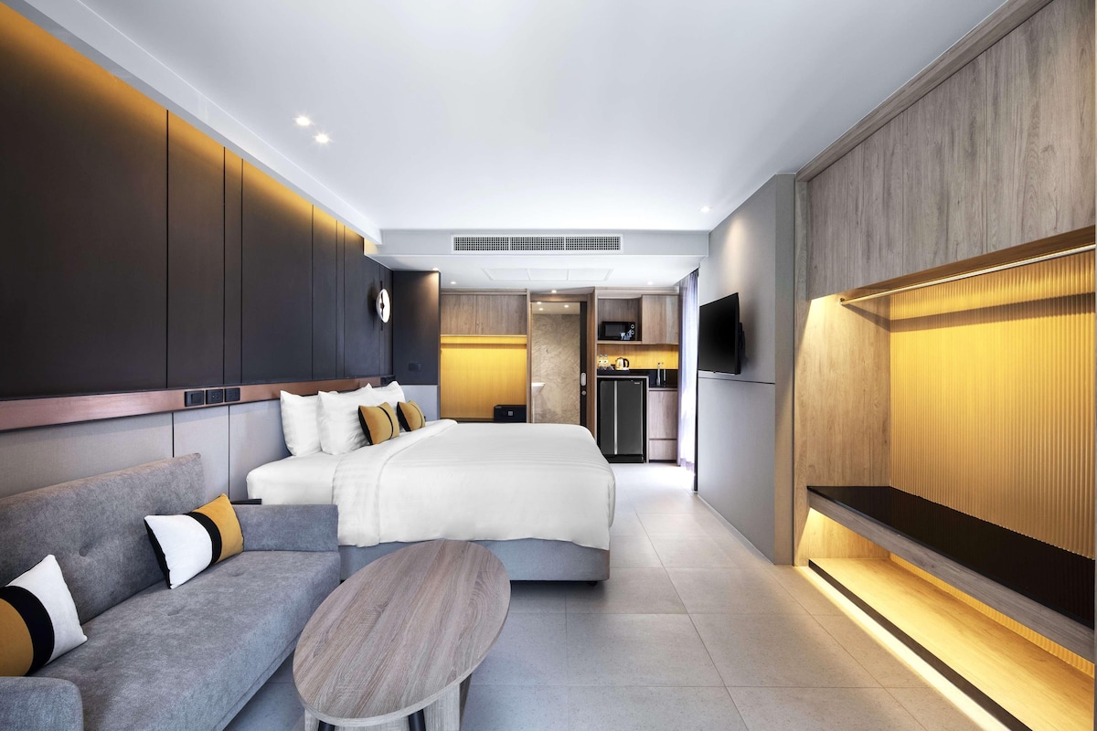 A modern hotel room with a bed, sofa, and a small table.