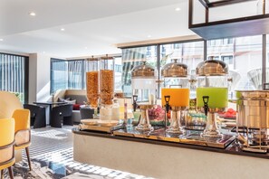 A modern bar area with a glass counter, various drink dispensers, and seating arrangements.