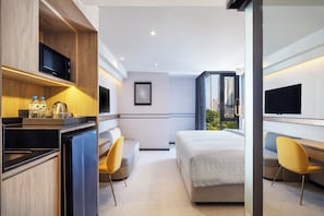 Une chambre d’hôtel moderne équipée d’un lit, d’une télévision, d’un bureau avec un micro-ondes, d’une chaise et offrant une vue sur la ville.