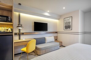A modern hotel room with a bed, a desk with a chair, a flat-screen TV mounted on the wall, and a microwave in the kitchenette area. - Best Western Ratchada Hotel (Bangkok)