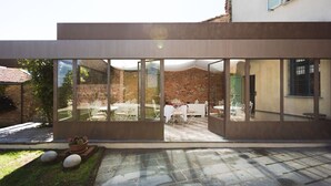 Un patio moderno al aire libre con paredes de vidrio, una pared de ladrillo y una mesa blanca dispuesta para comer.