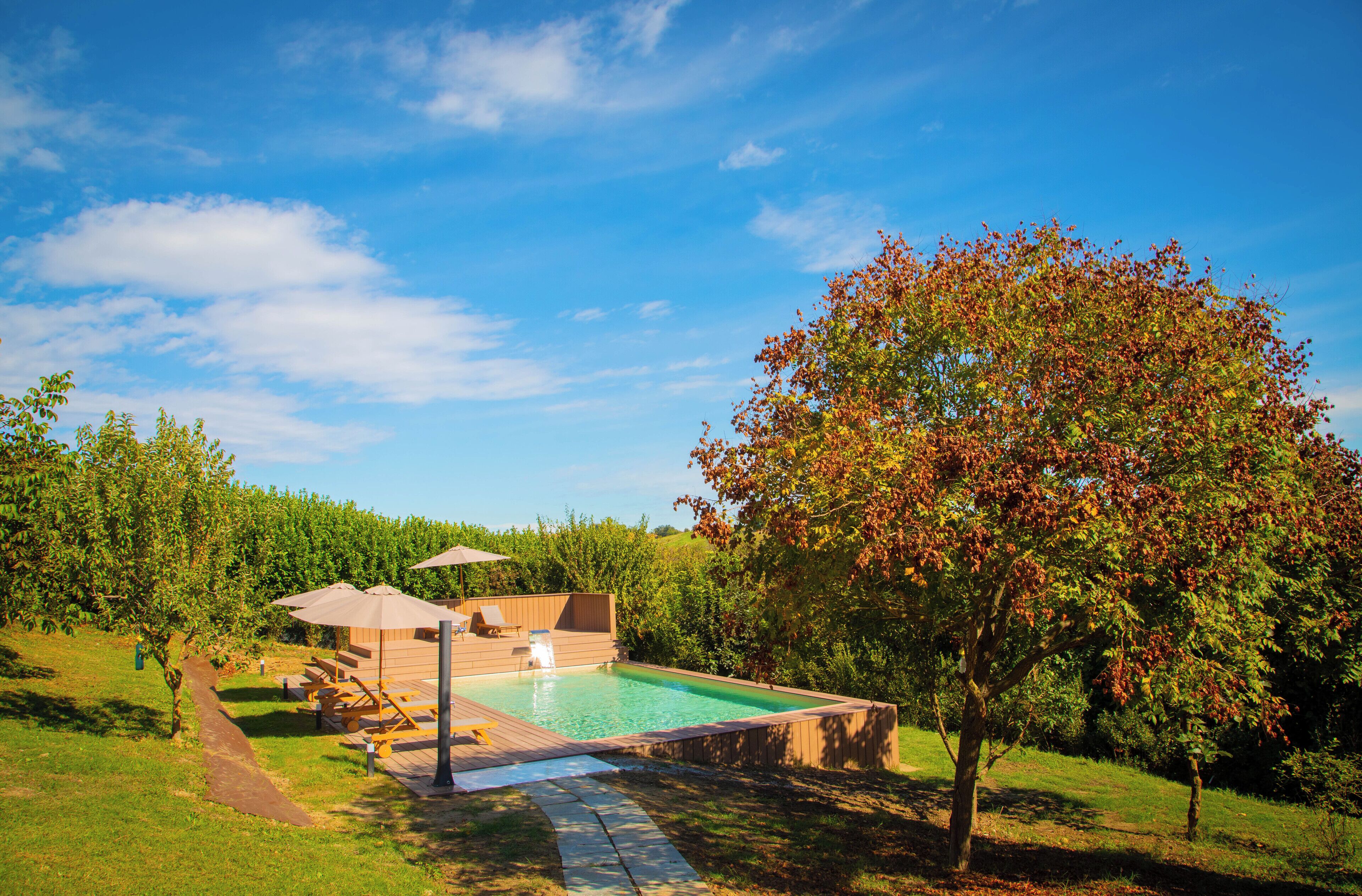 A swimming pool with a wooden deck, lounge chairs, and a hot tub.